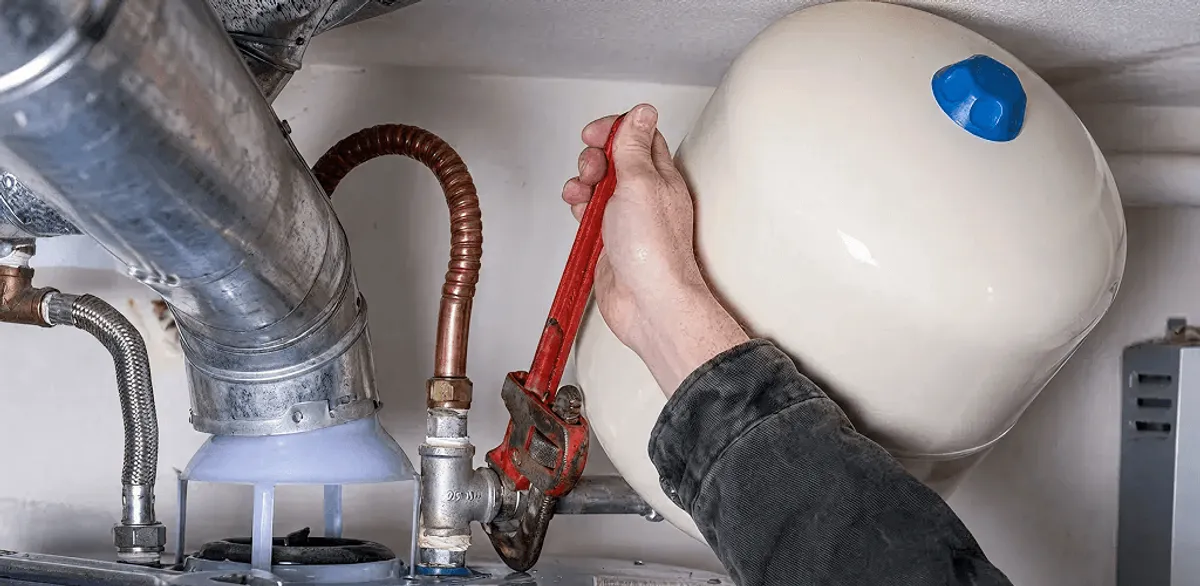 Water heater repair technician tightening plumbing connections near a tank unit in Portland, OR